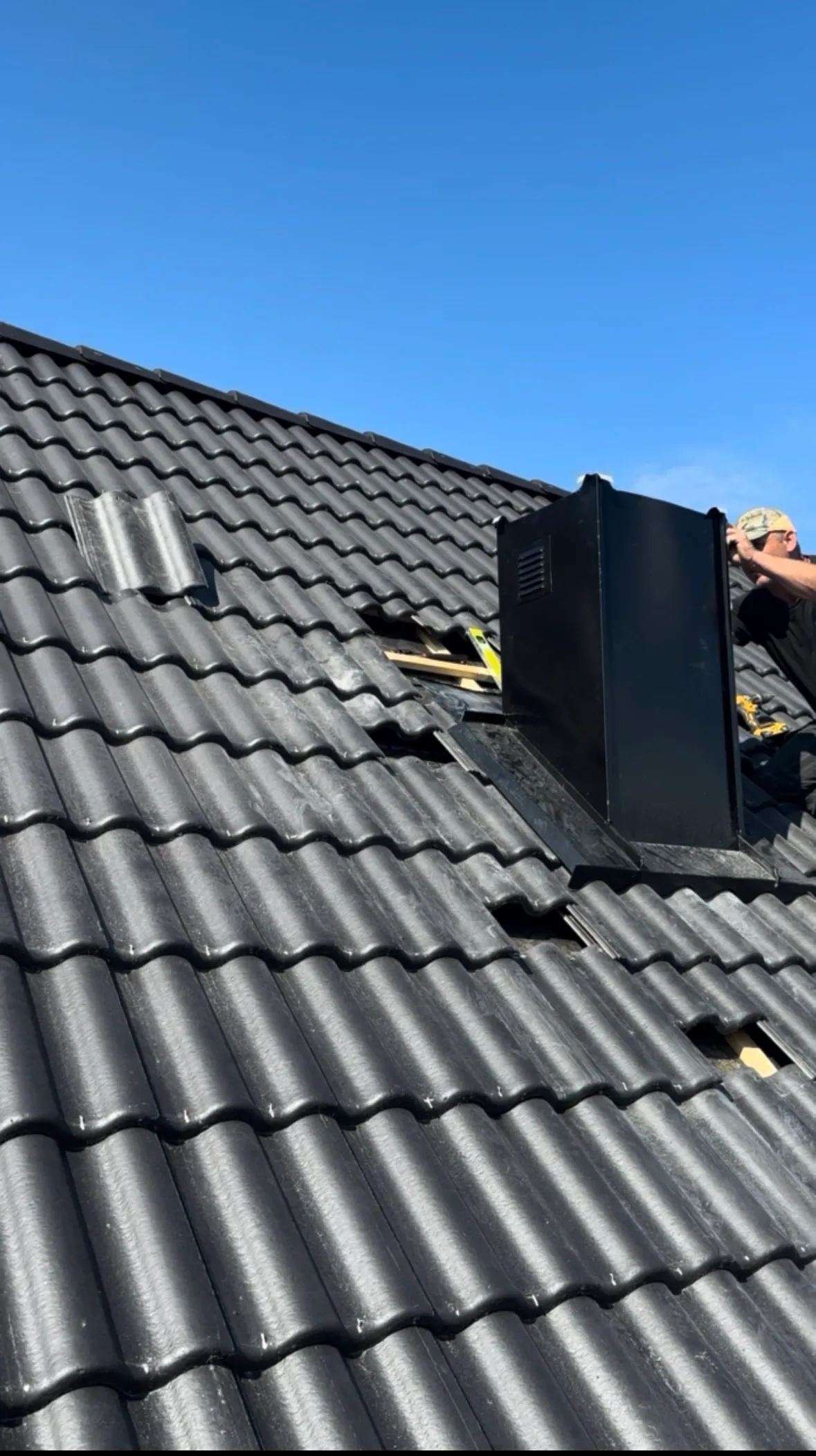 Svart ventilationshuv och plåtbeslag som monteras i ett nylagt betongpannetak