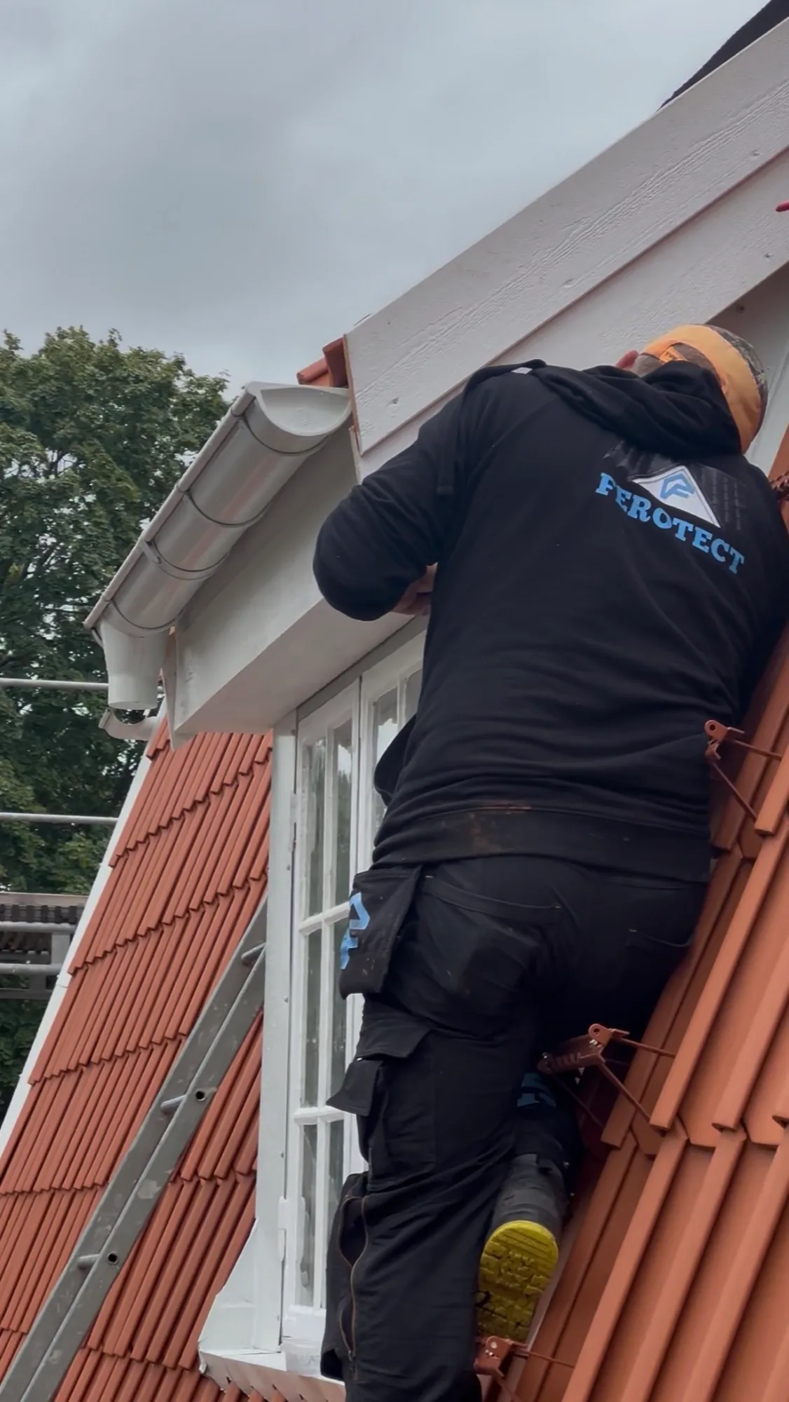 Montör i Ferotect-tröja som arbetar vid takfot och hängränna på ett tegeltak